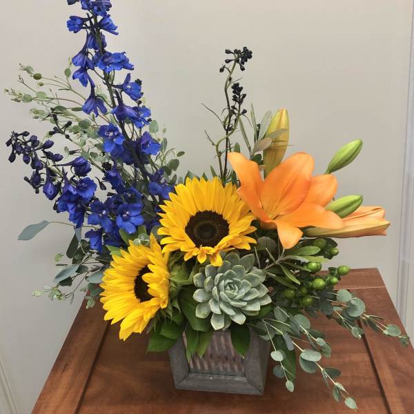 Bright mixed flower arrangement in a wooden box with sunflowers, lilies, and blue blooms