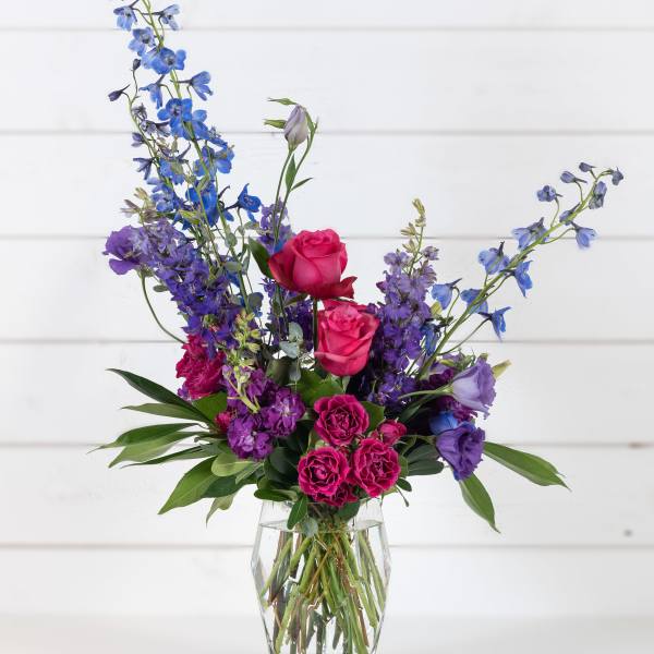 Mixed bouquet of pink roses and blue-purple flowers in a clear glass vase