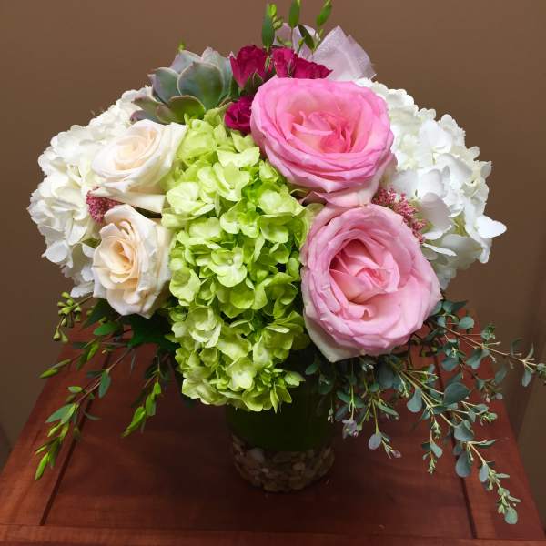 Round bouquet of pink roses, white and green hydrangeas, and a succulent in a glass vase