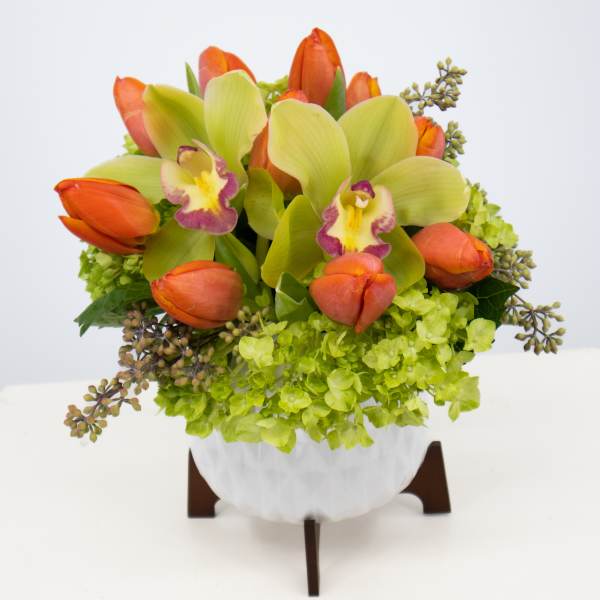 Orange tulips and green orchids in a white vase