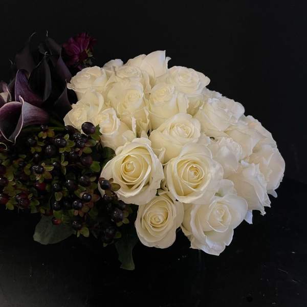 Low arrangement of white roses with dark purple calla lilies and berries.