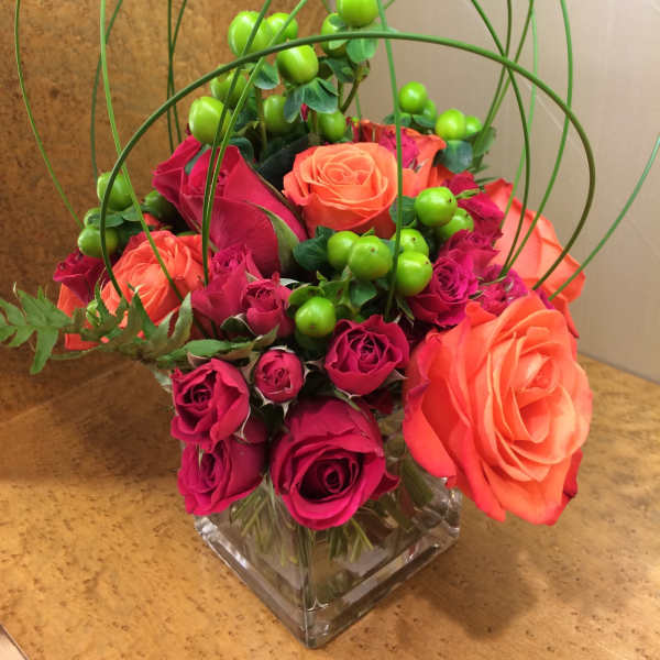 Pink and orange roses in a square glass vase with green berry accents