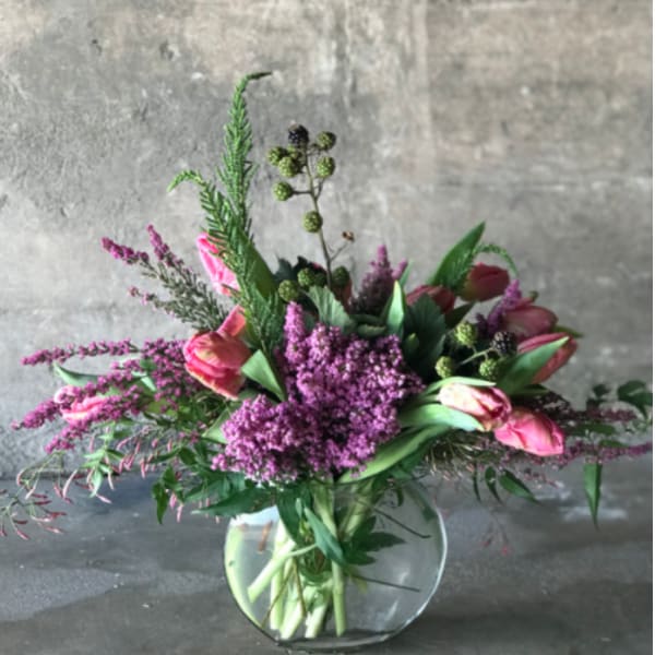 Pink tulips and purple flowers arranged in a clear glass vase
