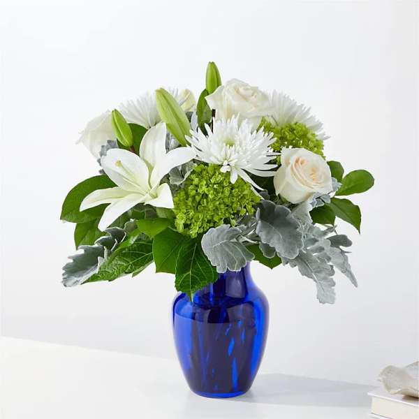 White lilies and roses arranged in a blue glass vase