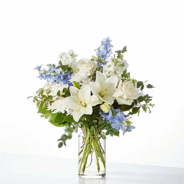 White lilies and roses with blue flowers in a clear glass vase
