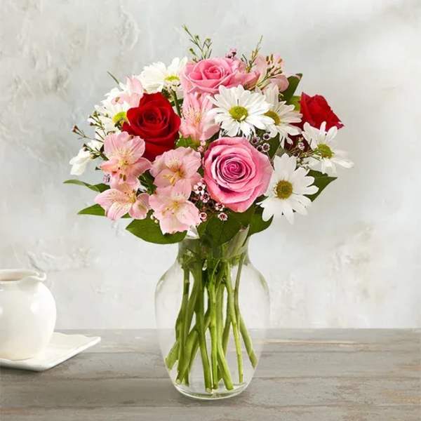 Pink and red roses with white daisies in a clear glass vase