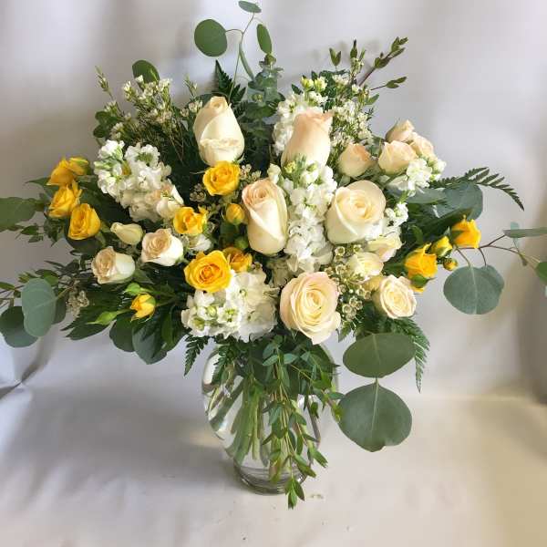 Cream and yellow roses in a clear glass vase with greenery