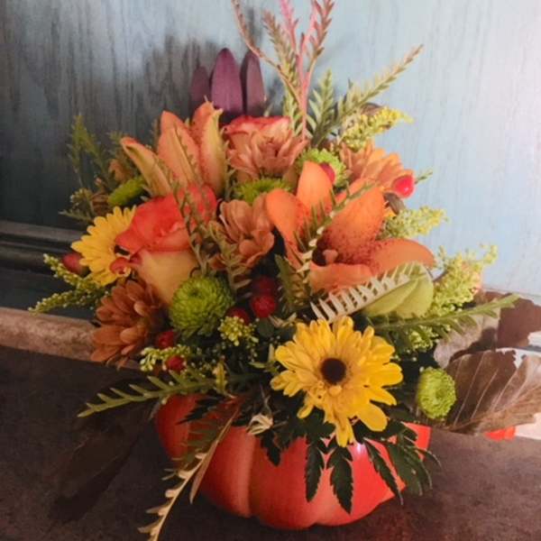 Autumn bouquet in an orange pumpkin container with yellow daisies and orange blooms