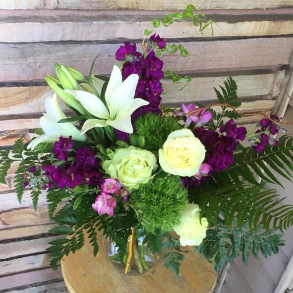Bouquet of white lilies, pale roses, and purple flowers in a vase