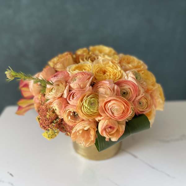 Round bouquet of peach and yellow flowers in a gold vase
