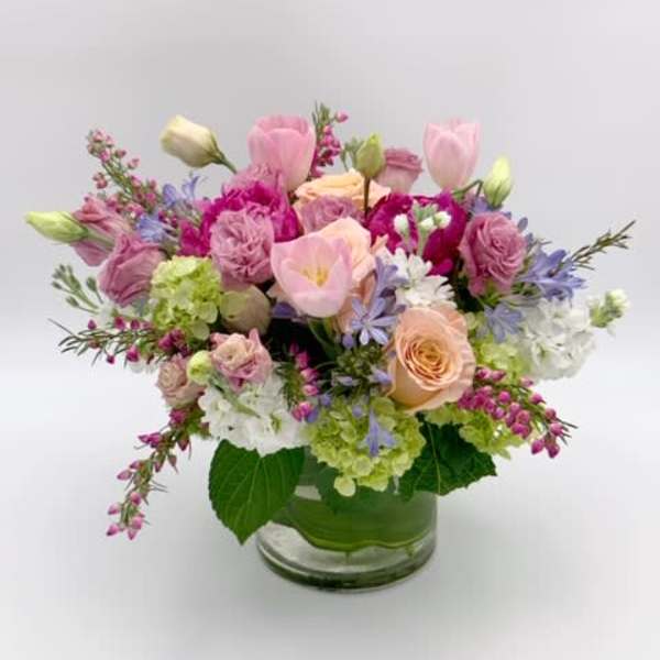 Low glass vase arrangement with pink tulips, roses, hydrangeas, and other pastel flowers