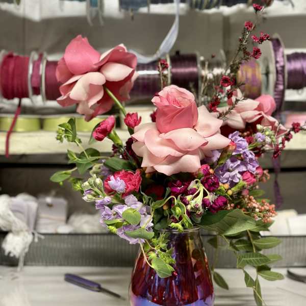 Pink rose bouquet in a purple glass vase with lavender flowers