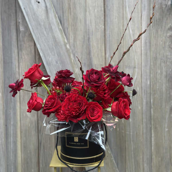 Red roses arranged in a black hat box with clear wrap