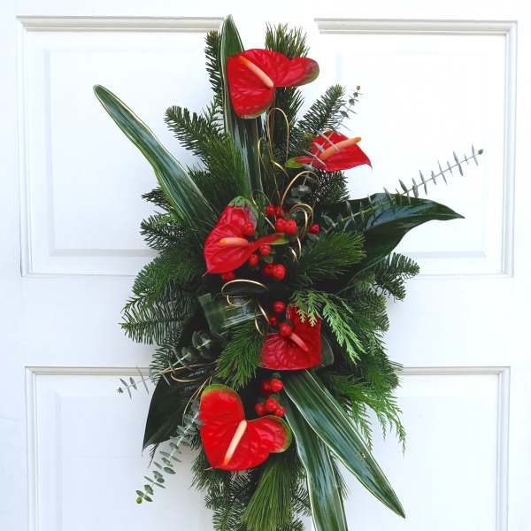 Red anthuriums and evergreen foliage arranged on a door wreath.
