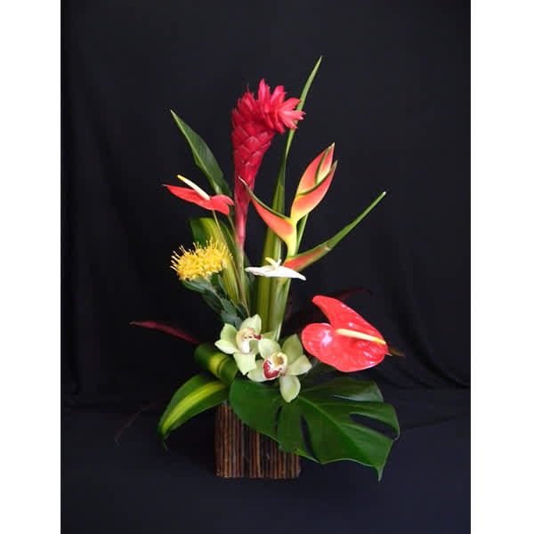 Tropical floral arrangement with red and orange blooms in a tall container