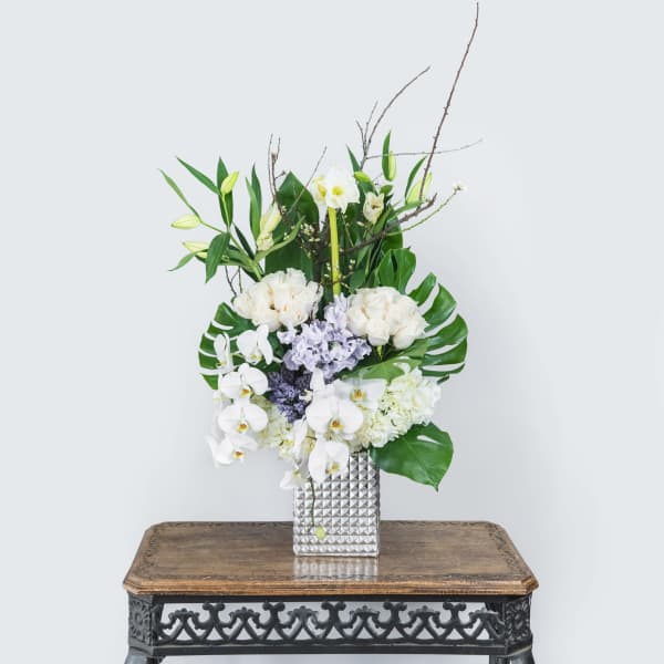 White orchids and lilies arranged in a silver vase on a table