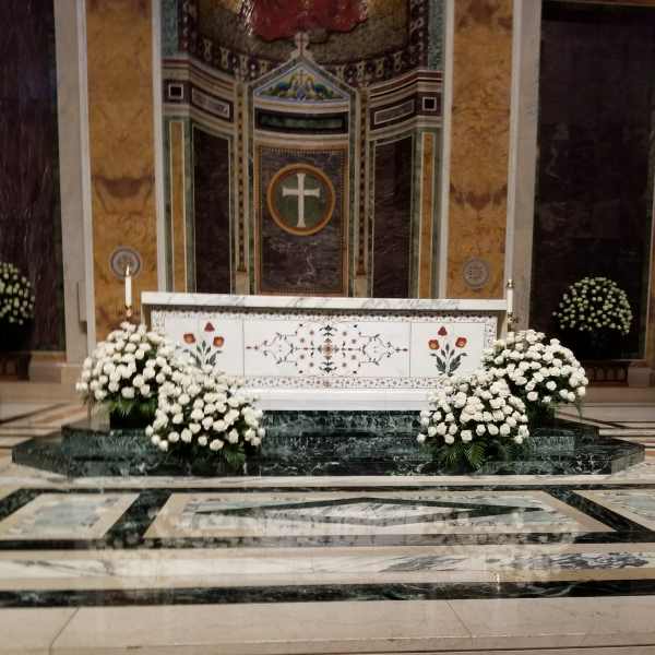 White floral arrangements on a church altar with a cross backdrop