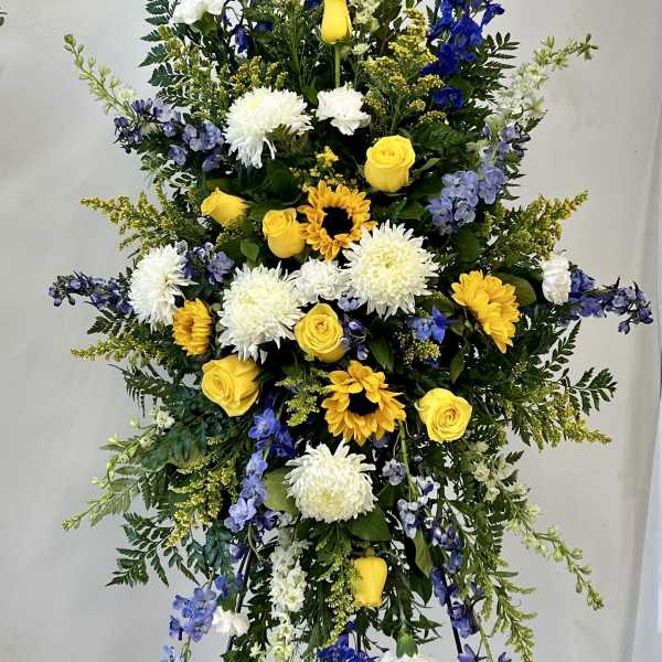 Tall standing floral spray with yellow roses, white mums, and blue delphinium