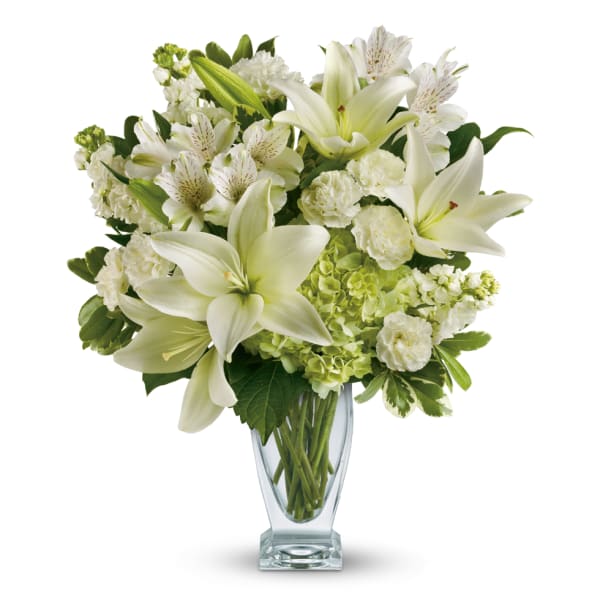 White lilies and mixed white flowers in a clear glass vase