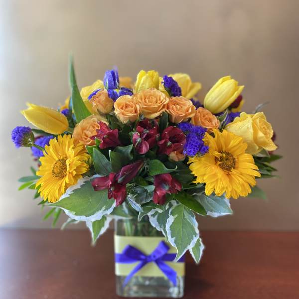 Mixed bouquet of yellow, orange, and purple flowers in a glass vase