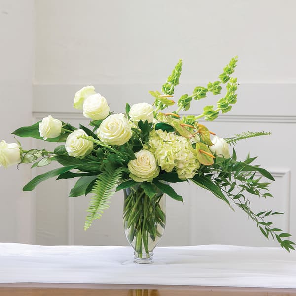 White roses and green flowers in a clear glass vase