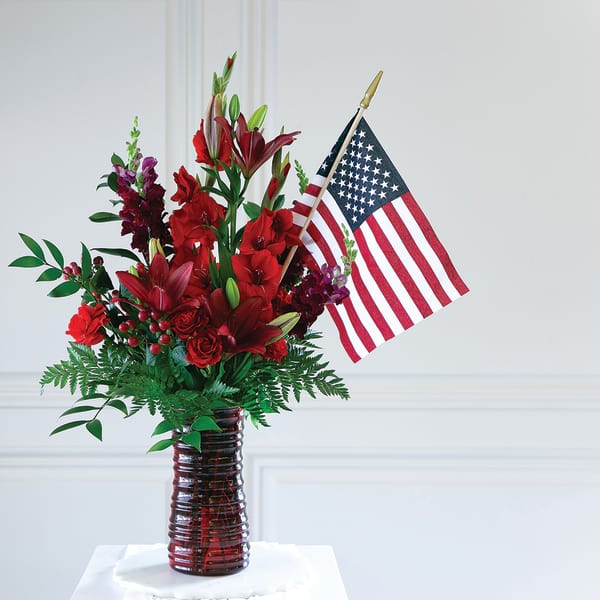 Red floral arrangement in a glass vase with an American flag