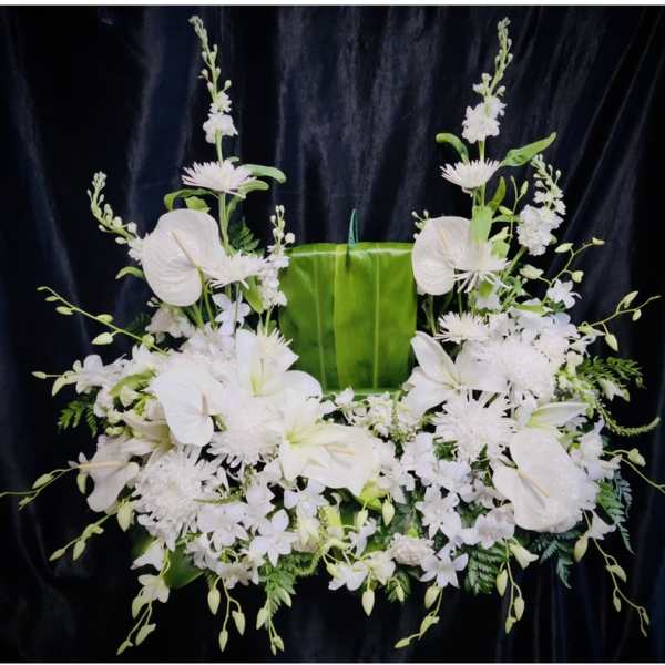 White floral funeral spray with lilies and orchids on a green backdrop