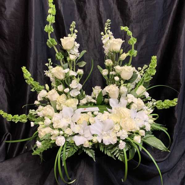 Large white floral arrangement with roses and orchids on a black backdrop