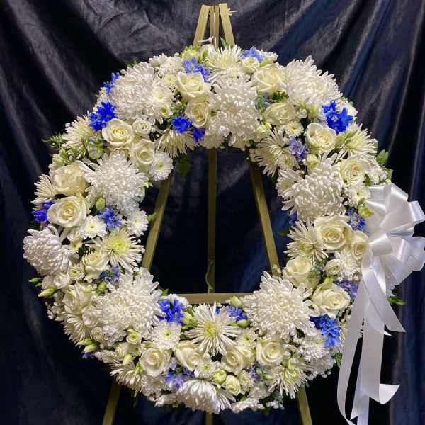 White floral wreath with blue accents on a wooden easel and white ribbon