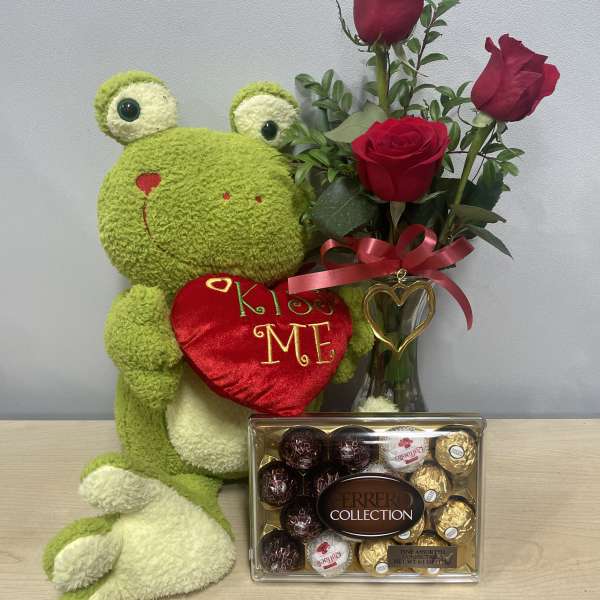 Stuffed frog holding a heart beside red roses and a box of chocolates