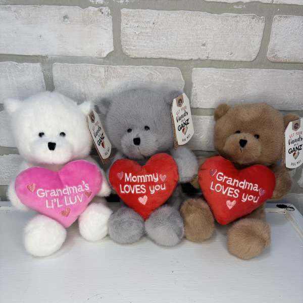 Three plush teddy bears holding heart pillows with love messages
