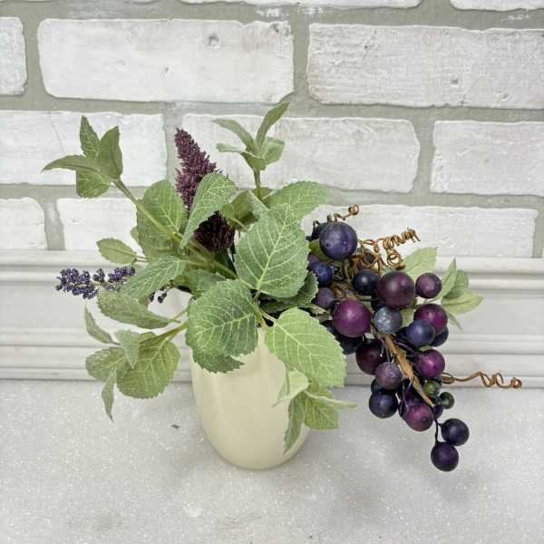 Small faux floral arrangement with purple berry clusters in a cream vase