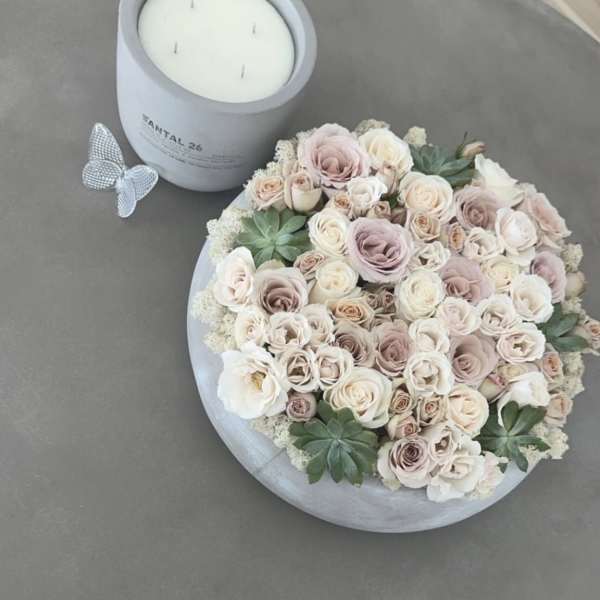 Round box of pale roses beside a white candle jar