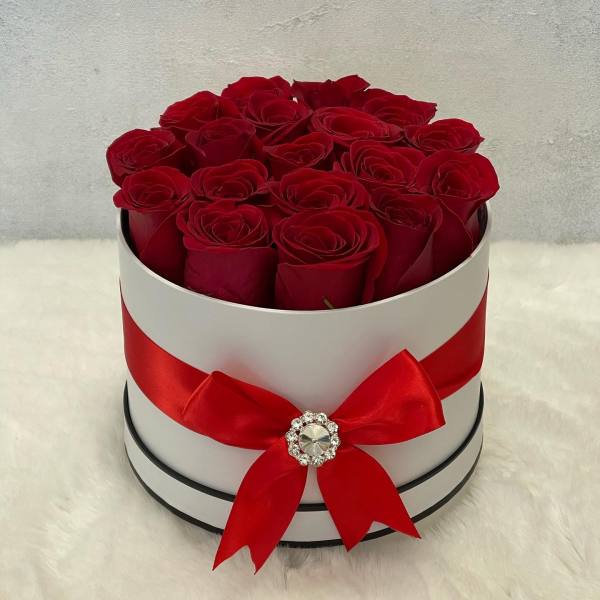 Round white hatbox of red roses with a red ribbon bow on a soft white surface