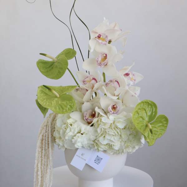 White orchid arrangement with green anthuriums in a white vase