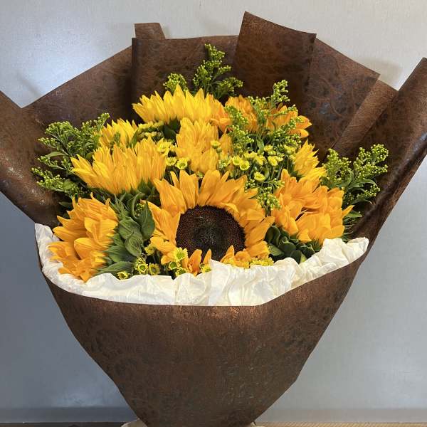 Bouquet of yellow sunflowers wrapped in brown paper with a beige bow