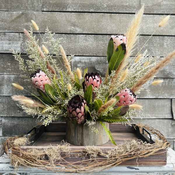 Pink protea arrangement in a wooden container with dried grasses