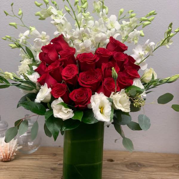 Red roses and white flowers arranged in a green glass vase