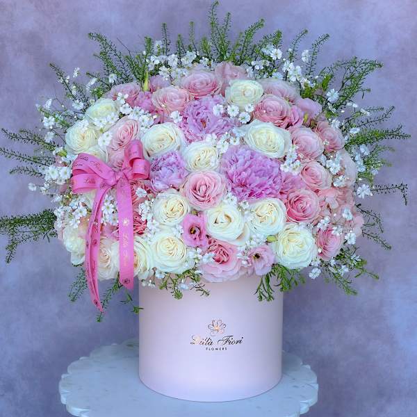 Pink and white roses arranged in a round hatbox with a ribbon