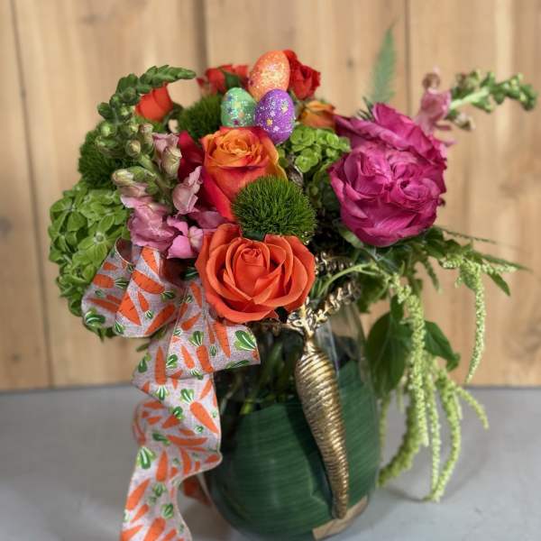 Colorful bouquet of roses and greenery in a green vase with a carrot-print ribbon
