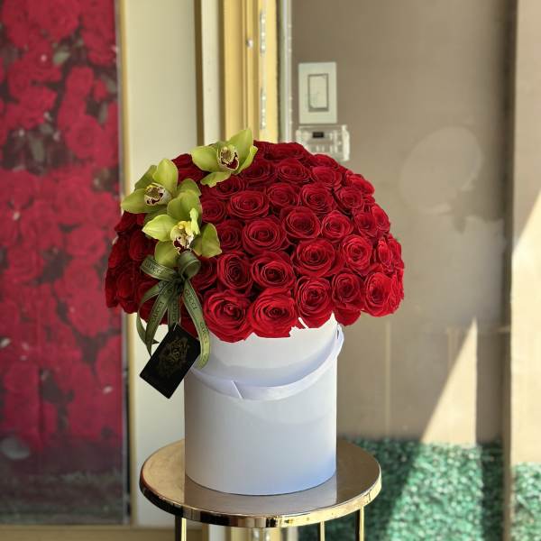 Round bouquet of red roses with green orchids in a white box