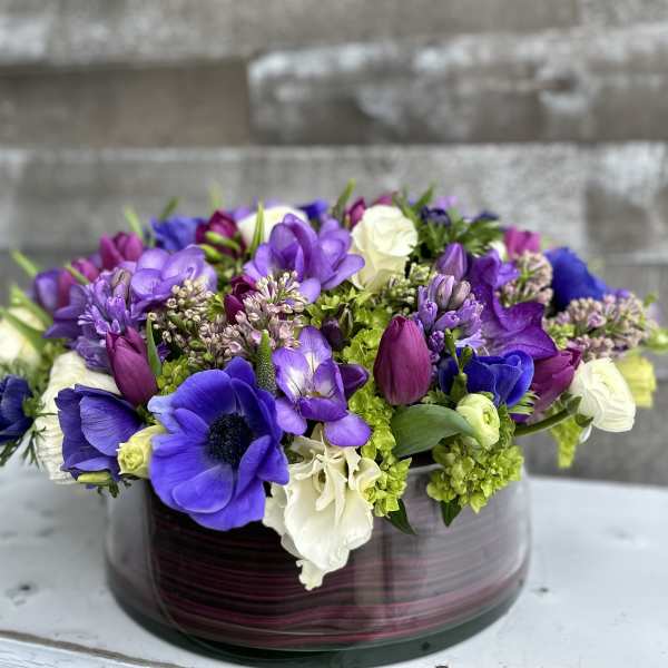 Purple and white mixed flower arrangement in a round glass vase