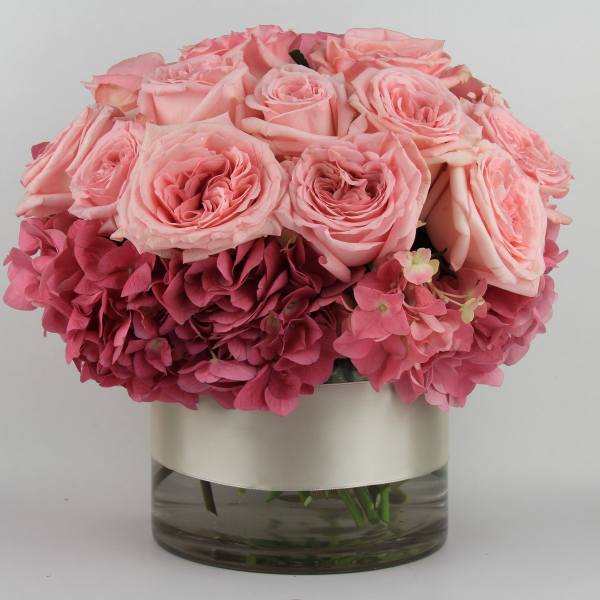 Pink roses and hydrangeas arranged in a glass vase with a ribbon band