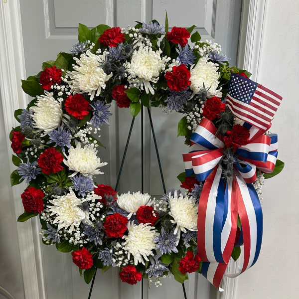 Red, white, and blue floral wreath on a stand with an American flag ribbon