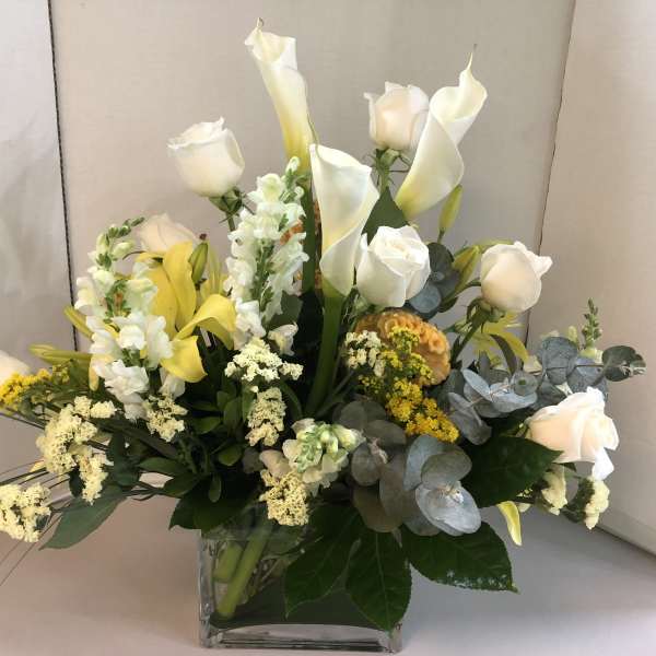 White roses and calla lilies arranged in a clear square vase