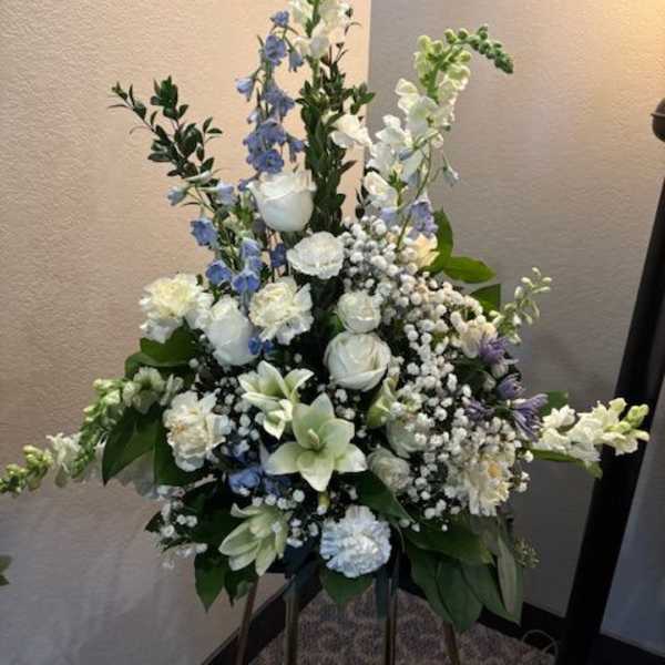 Tall white and blue floral funeral spray on a stand