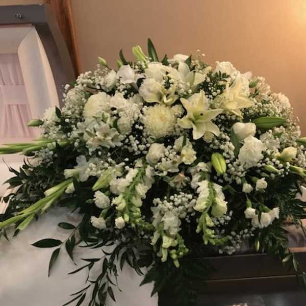 Large white funeral casket spray with lilies and baby’s breath