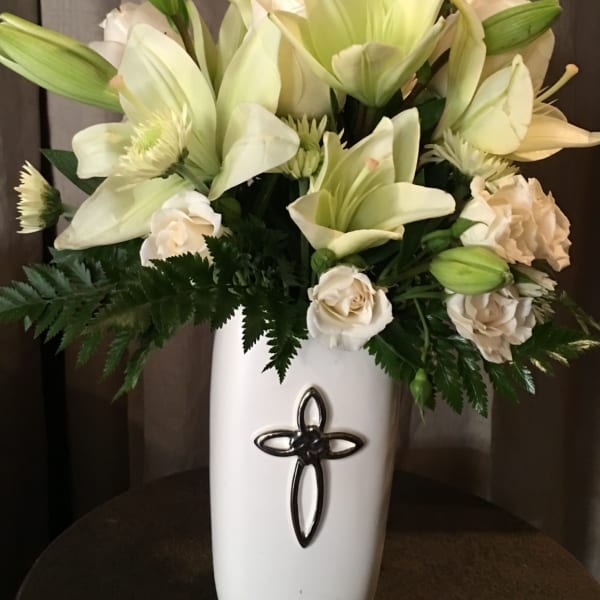 White lilies and cream roses in a tall white vase with a cross emblem