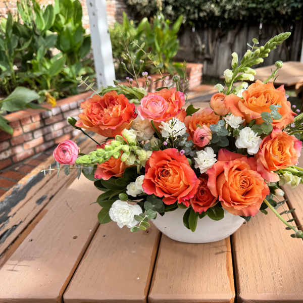 Orange and pink rose arrangement in a white bowl vase