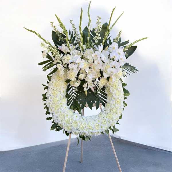 White floral standing wreath on an easel with orchids and chrysanthemums